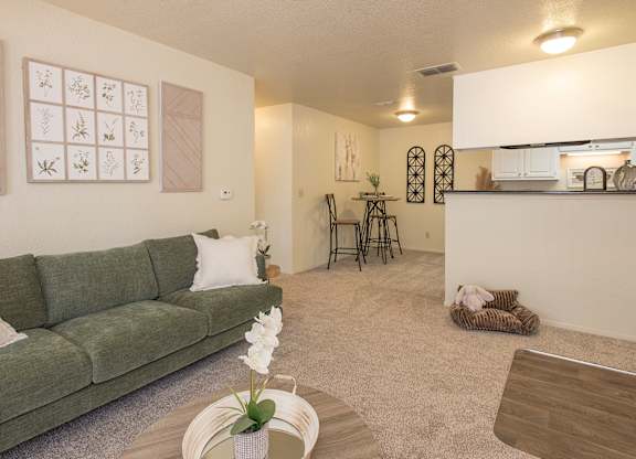A living room with a green couch and a coffee table with a vase of flowers on it at Zinfandel Village Apartments, California, 95670