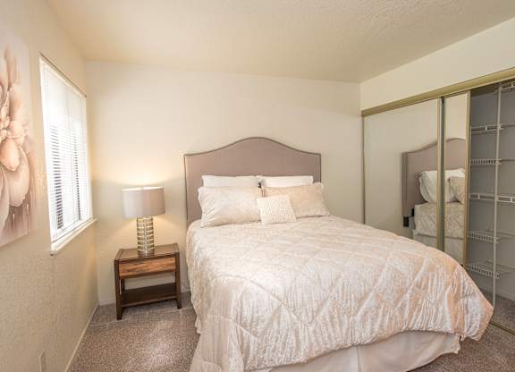 A bedroom with a bed, nightstand, and a mirror at Zinfandel Village Apartments, California, 95670