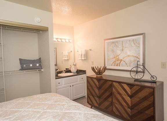 A bedroom with a bed, vanity, and a painting on the wall at Zinfandel Village Apartments, California, 95670