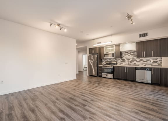 an empty living room and kitchen with wood flooring and a stainless steel refrigerator