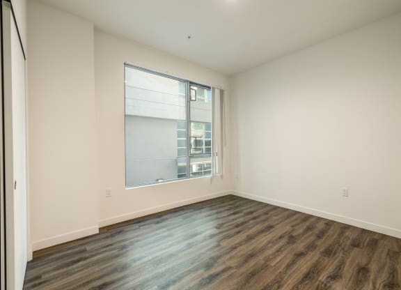 an empty living room with a large window and wood flooring