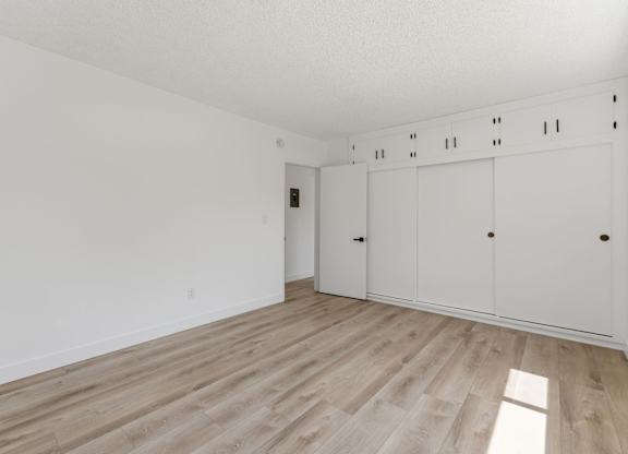 A room with a white wall and a wooden floor with a white cabinet.