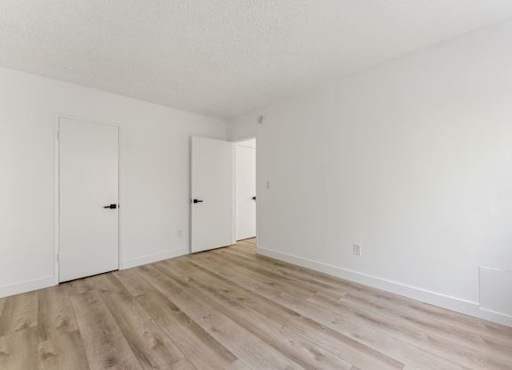A room with white walls and wood flooring with three doors.