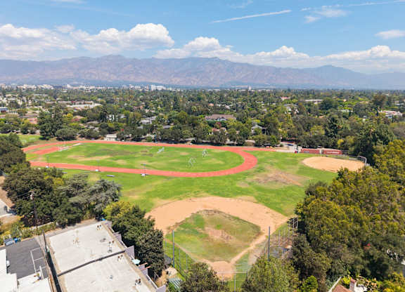 A large, open park with a baseball field and a soccer field, surrounded by trees and buildings.