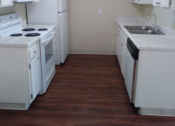 Kitchen with dark hardwood flooring and white kitchen appliances and cabinets at Teton Pines Apartments in Escondido, California.