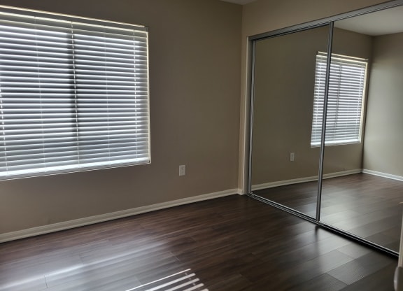 Bedroom with plank style flooring, large window and large closet with sliding mirror doors at The Cove at Bear Valley in Escondido, California.