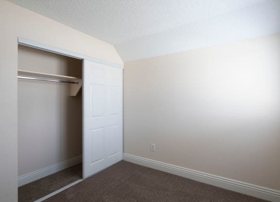 Carpeted bedroom with large closet and window at the Atrium Apartments in San Diego, California.