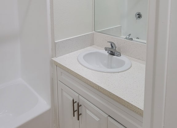 Bathroom sink with white cabinets and large mirror in one bedroom apartment at the Atrium Apartments in San Diego, CA.
