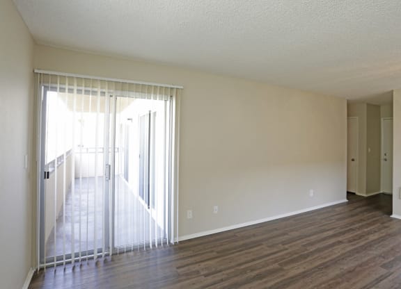Living room with plank style flooring and sliding glass doors to private porch at Villa Pacific Apartments in Oceanside, California.
