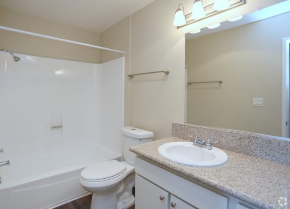Bathroom with white fixtures and vanity with white cabinets in unit at Villa Pacific Apartments in Oceanside, California.