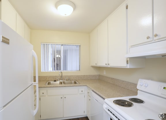 Kitchen with white appliances including refrigerator, dishwasher, and electric range at Villa Pacific Apartments in Oceanside, California.