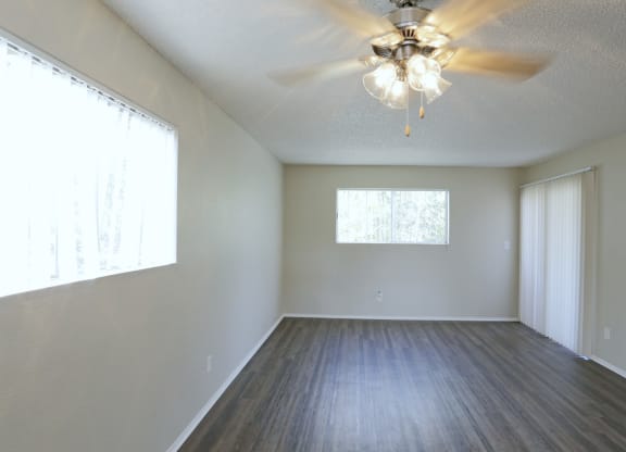 Dining araa with ceiling fan and living room with plank style flooring and lots of windows for natural light at Villa Pacific Apartments in Oceanside, California.