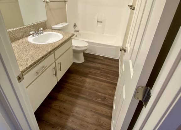 Bathroom with plank style flooring, white vanity cabinets and white fixtures in unit at Villa Pacific Apartments in Oceanside, California.