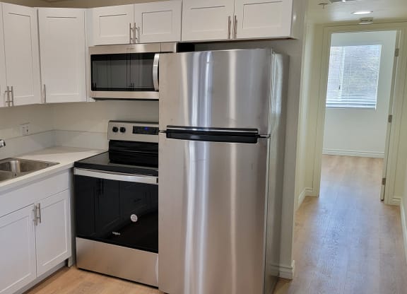 Well lit kitchen with white cabinets and new appliances and hallway to bathroom and bedroom at the Atrium Apartments in San Diego, CA.
