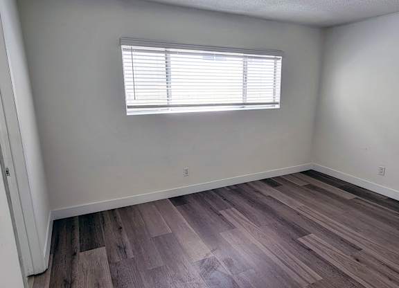 A room with wooden flooring and a window with blinds.