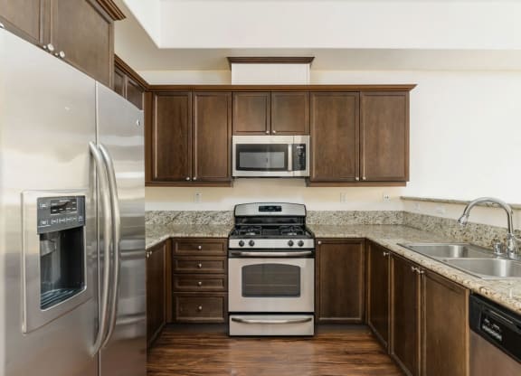 Kitchen with stainless steel appliances, granite slab counter tops, and spacious dark wood cabinets at The Nines Townhomes in Escondido, California.