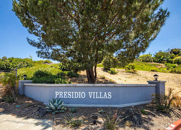 A sign that says "Presidio Villas" in front of a tree.