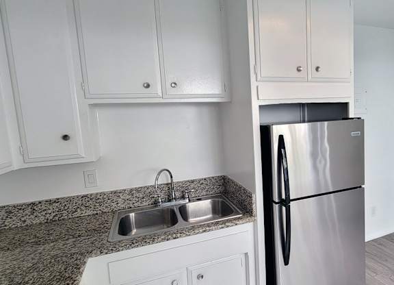 A kitchen with a granite countertop and a stainless steel refrigerator.