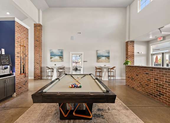A pool table is in the middle of a room with a brick wall.