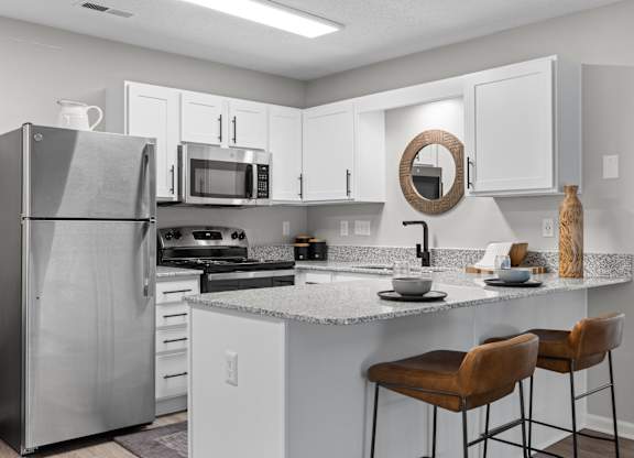 A kitchen with a refrigerator, microwave, oven, and bar stools.