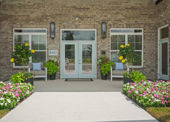 the front of a brick building with doors and a sidewalk with flowers