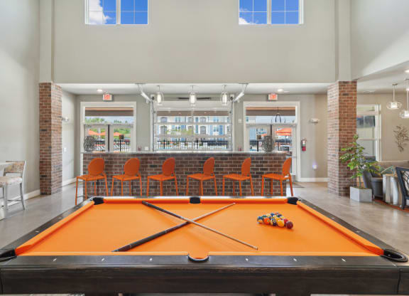 a pool table in a clubhouse with a bar in the background