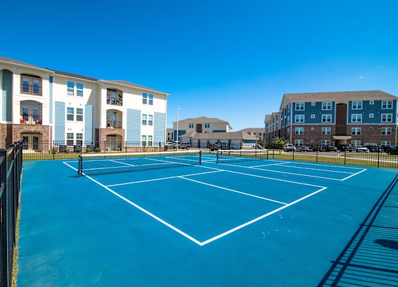 A tennis court is surrounded by apartment buildings.