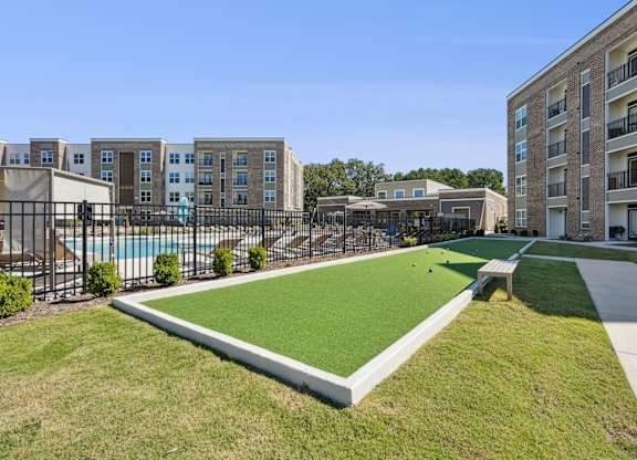 A grassy area in front of apartment buildings with a pool and a small pavilion.