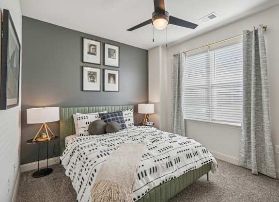 A bedroom with a bed, two lamps, and a ceiling fan.