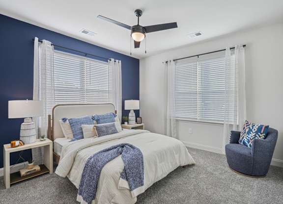 A bedroom with a bed, chair, and ceiling fan.