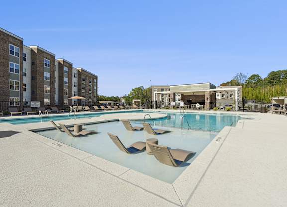 A large swimming pool with lounge chairs in front of apartment buildings.