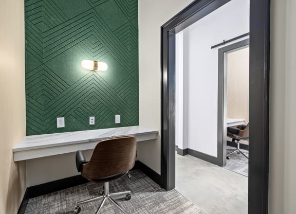 a room with a desk and a chair in front of a wall with green wallpaper