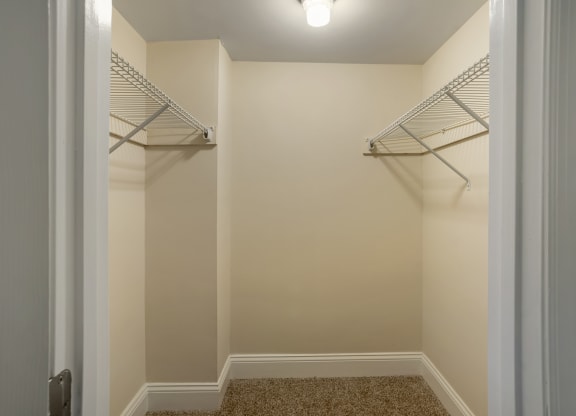 a walk in closet in a home with white walls and shelves and a white door