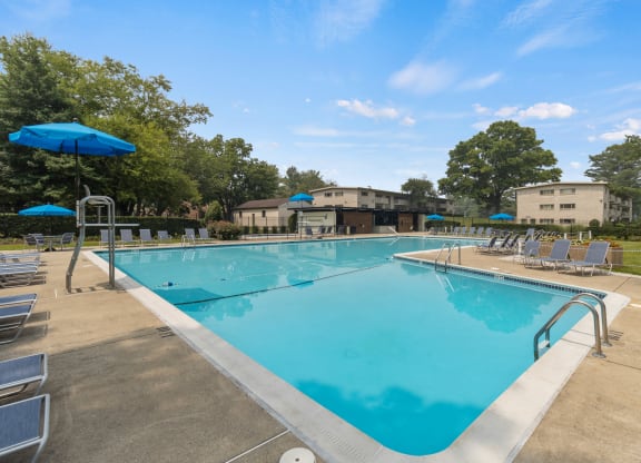 a swimming pool with chairs and umbrellas and buildings in the background