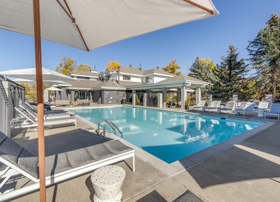 a swimming pool with chairs and umbrellas in front of a house