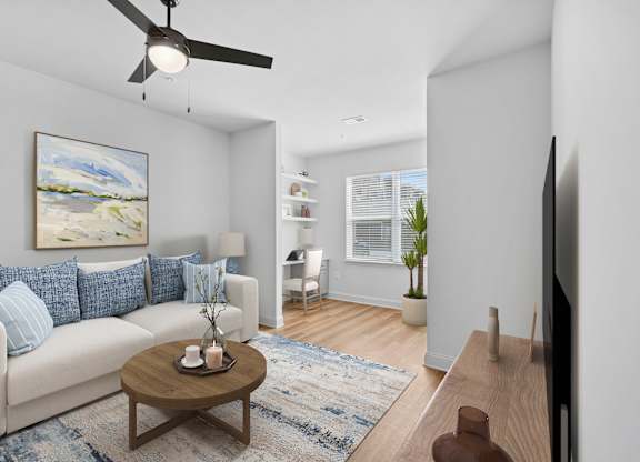 A living room with a white couch, a painting on the wall, a ceiling fan, and a coffee table with candles on it.
