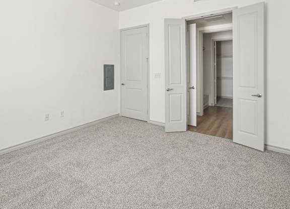 A room with white walls and carpeted floor with two doors.