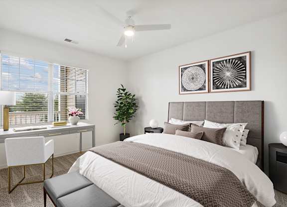 A bedroom with a large bed, a desk with a chair, and a potted plant.