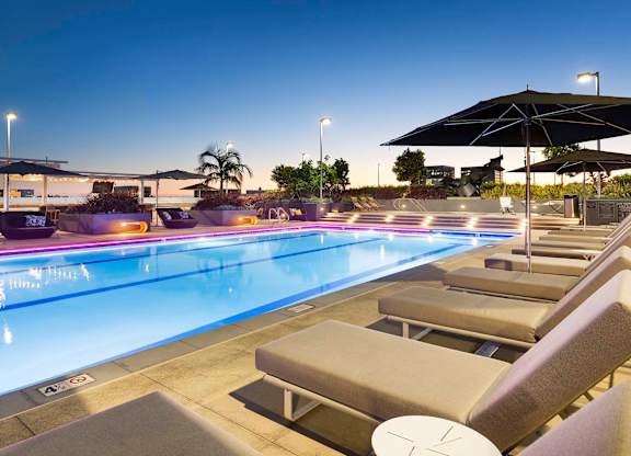 Rooftop pool deck at twilight with illuminated water at Elements Apartments, Irvine