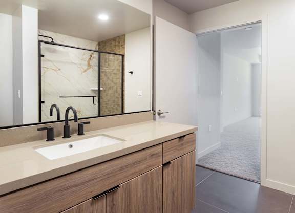 Bathroom vanity with wood cabinetry and black fixtures at Elements Apartments, California