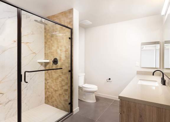 Bathroom with glass enclosed shower and textured tile accent at Elements Apartments, California, 92612