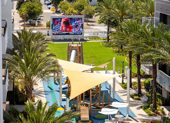 Community courtyard with playground and large outdoor screen at Elements Apartments, California, 92612