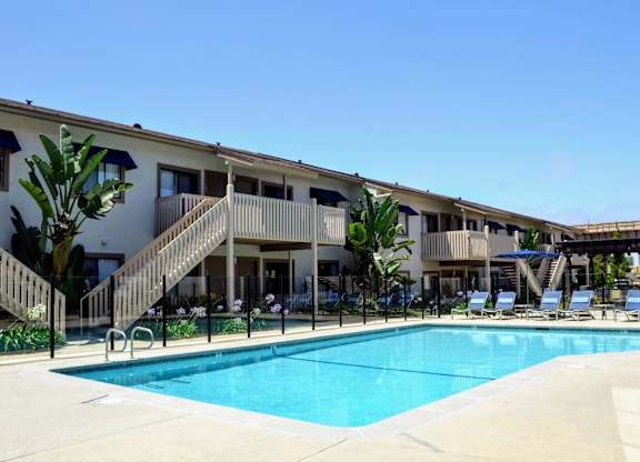 A swimming pool is surrounded by sun loungers and palm trees.at La Jolla Canyon Apartments, San Diego, CA 92121