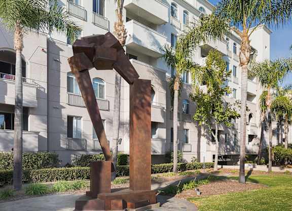 Rusted steel sculpture among palm trees and greenery at La Jolla Crossroads Apartments, San Diego, CA