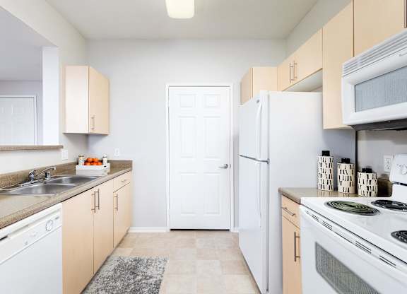 Galley kitchen with white appliances and light wood cabinets at La Jolla Crossroads Apartments, California