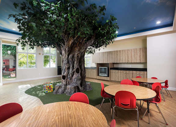 Indoor play area with artificial tree and round tables at La Jolla Crossroads Apartments, California