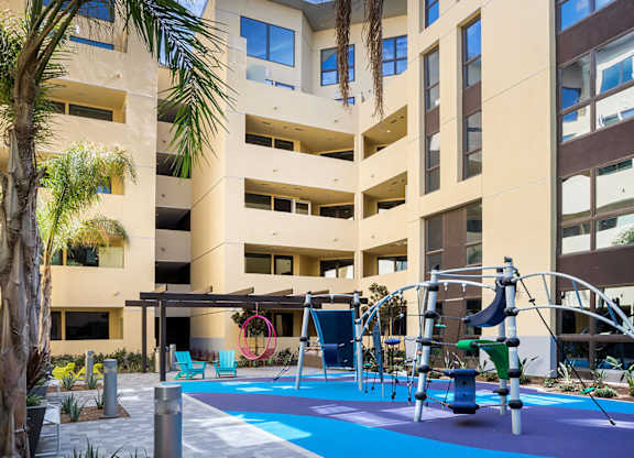 Outdoor courtyard playground with colorful equipment and palm trees at Metropolis Apartments, IRVINE, CA 92614