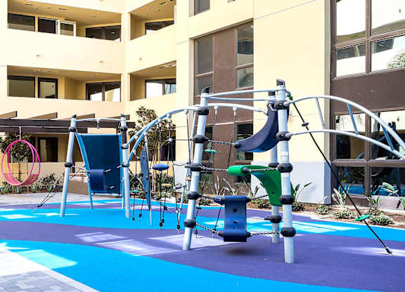 Childrens play area with climbing structure and blue surfacing at Metropolis Apartments, IRVINE, CA