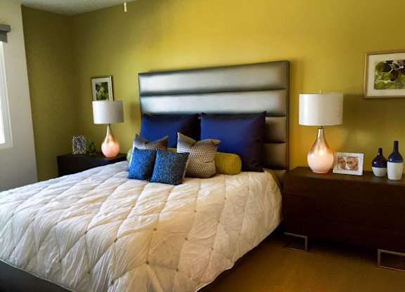 Bedroom with upholstered headboard and yellow accent wall at Torrey Gardens Apartments, California
