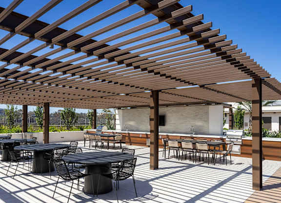 A rooftop lounge with barbeques, tables, and TV's under a wooden cabana.